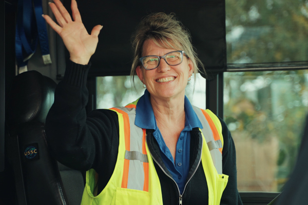 female bus driver waves from drivers seat