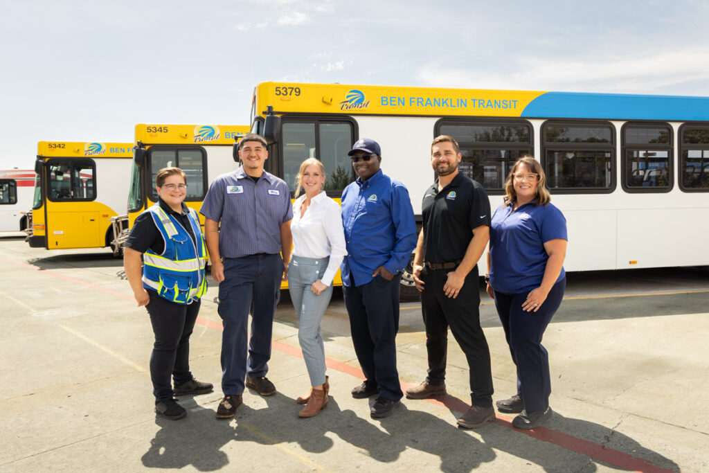 Six BFT staff members smile in front of a bus.